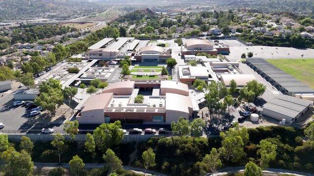 Santa Clarita junior high school buildings, sports fields, modern layout, abundant greenery, and suburban landscape under sunny daylight - ascending aerial reveal
