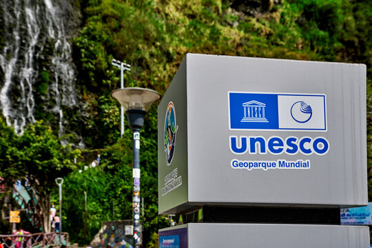 Banos De Agua Santa, Ecuador - March 28, 2026: Official sign UNESCO Global Geoparks Network against backdrop waterfall in city of Banos de Agua Santa, part of Tungurahua Volcano UNESCO Global Geopark.