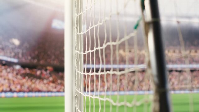 Selective focus of goal net rope and side post filling foreground with blurred soccer pitch, crowd stands and soft stadium light behind.