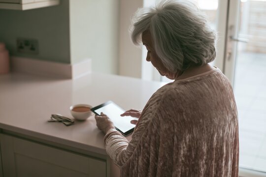Over-the-shoulder view of woman with tablet at pale kitchen counter