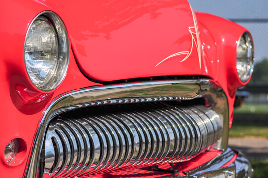 Close-up of the front grille and headlight of a classic red vintage automobile displayed at an outdoor car show in Oshawa, Ontario, Canada.