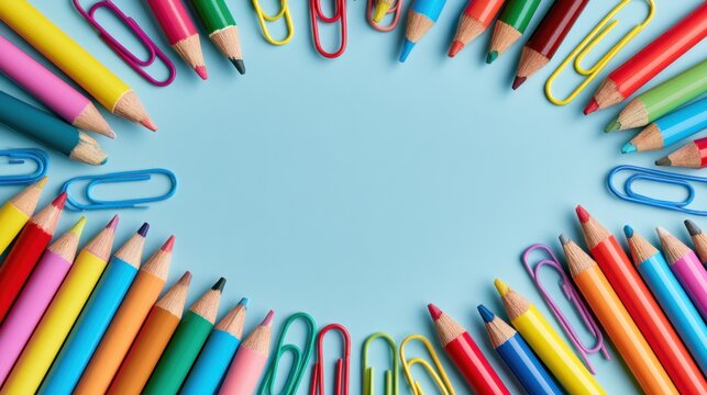 Vibrant assortment of colored pencils and paper clips arranged in a semi-circle on blue background with blank space in center for creative or educational concept