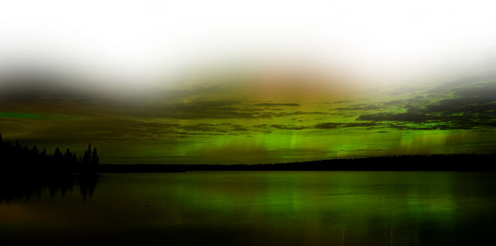 Wide view of an Aurora filled stary sky reflecting in a calm lake with a partially transparent sky. A night sky image.
