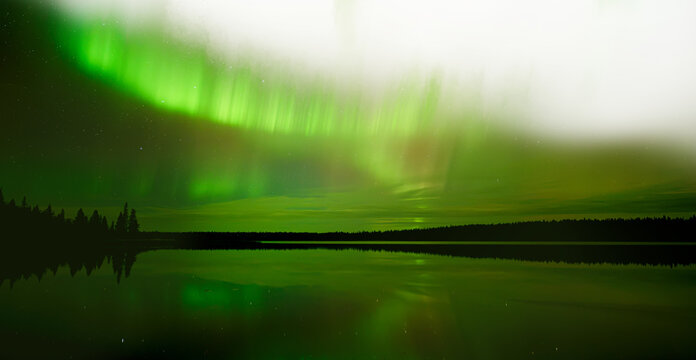 Wide view of an Aurora filled stary sky reflecting in a calm lake with a partially transparent sky. A night sky image.
