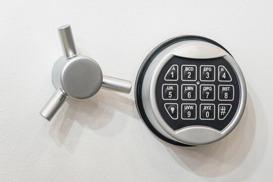 Close-up of a high-security electronic safe lock mechanism mounted on a white steel door. The setup features a digital alphanumeric keypad for passcode entry alongside a robust three-spoke manual hand