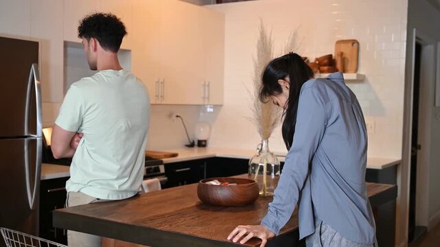 Couple standing apart in kitchen after argument with man looking away awkward