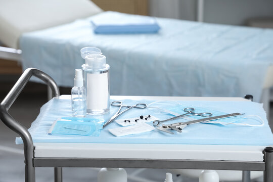 Body piercing tools and supplies on a medical cart in a sterile room with a bed in the background