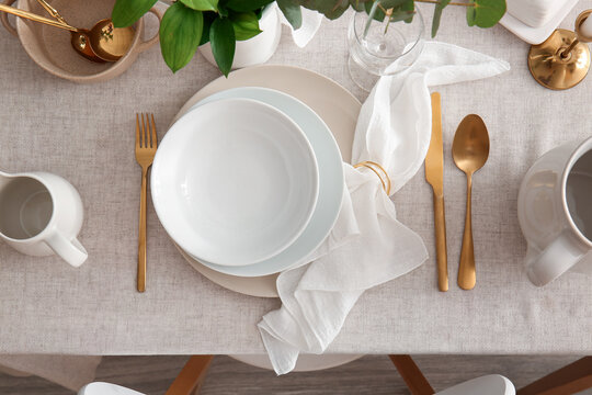 Elegant table setting with white plates gold cutlery and linen napkin on a light tablecloth top view for dining and hospitality