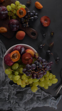 Assortment of fresh grapes plums and apricots in a white bowl and on a rustic wooden board