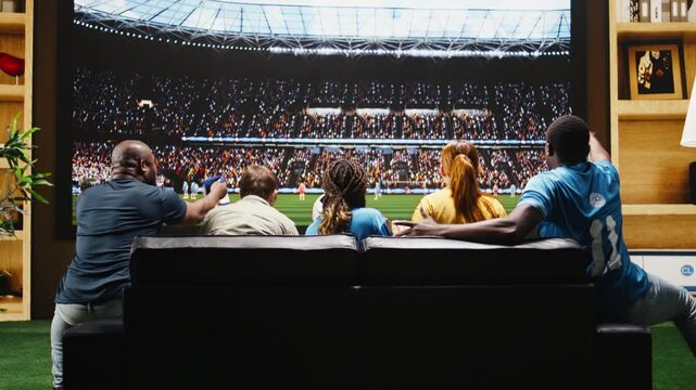 Football fans celebrate a goal at home during interactive TV viewing, with beer cups and sofa cheering creating a close-to-pitch stadium feeling.