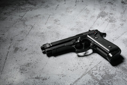 Black pistol handgun with a red safety indicator on a dark gray concrete background, crime and self-defense concept, the firearms metallic texture and the rough concrete surface create a stark