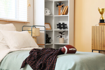 Teenage boys bedroom with a football on the bed, plaid shirt, and modern shelving unit with decor © Pixel-Shot