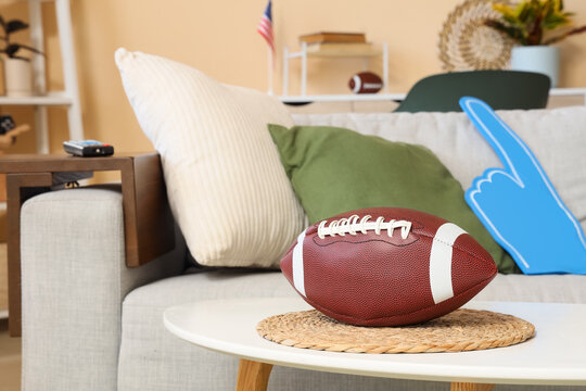 American football on a coffee table in a living room with a foam finger and flag, game day concept, a foam finger and an American flag are visible on the sofa