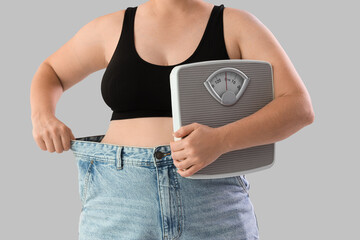 Overweight woman in loose jeans with scales on grey background