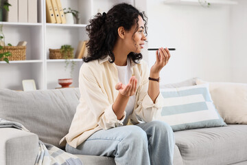Young African-American woman using mobile phone to search online on sofa at home