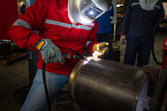 Professional welder using MIG torch on metal plate in industrial workshop.