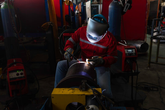 Professional welder using MIG torch on metal plate in industrial workshop.