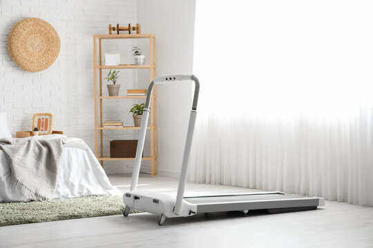 Interior of light bedroom with treadmill and shelf unit