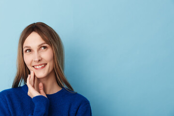 Obraz premium A fresh, friendly portrait of a smiling woman in a blue sweater inside a studio, posing closeup with a relaxed posture. Soft lighting highlights confidence and casual style in a bright, welcoming