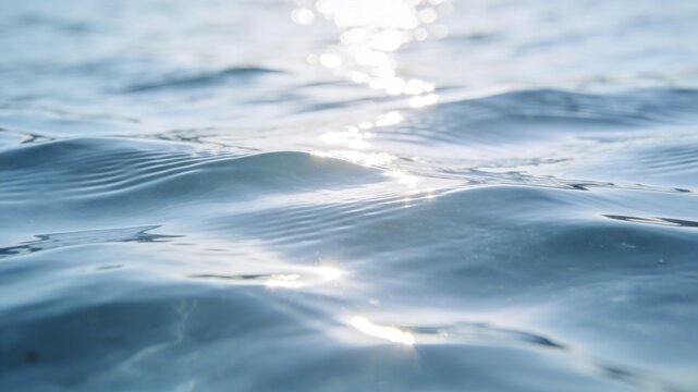 Serene blue water ripples glistening under bright sunlight, creating a shimmering effect on the calm ocean surface with soft bokeh reflections.