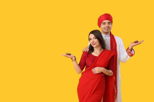 Beautiful Indian couple with diya lamps on yellow background
