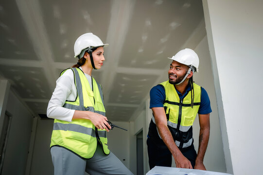Construction Manager analyzing building blueprint indoor with Civil engineer while holding walkie talkie, scene for real estate property development and professional engineering work at site
