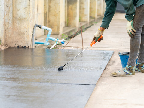 Professional construction worker applying a black waterproof coating onto a concrete slab surface