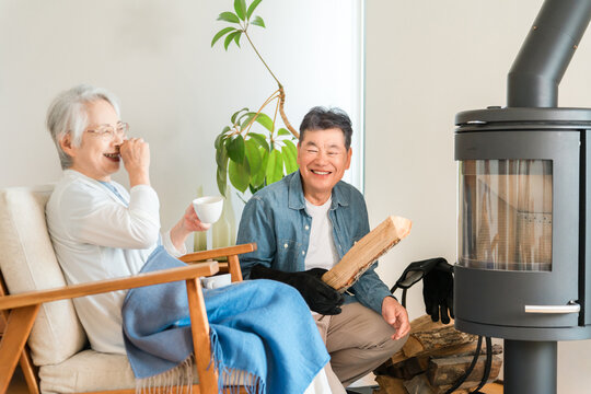 薪ストーブのあるマイホームのリビングで笑顔で会話するシニア夫婦