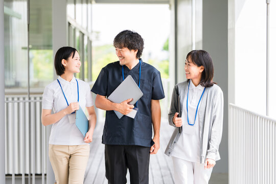 Care staff and medical staff, both male and female, wearing scrubs and polo shirts, walk down the corridors of a hospital or facility.