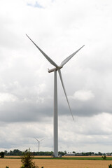 Fototapeta premium A modern wind turbine towers over rural land beneath a dramatic cloudy sky, symbolizing renewable energy, clean power, and sustainable electricity.