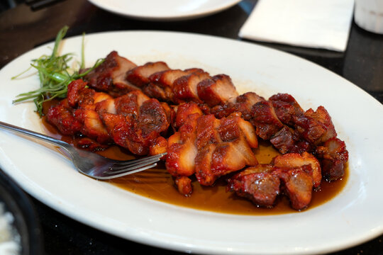 Chinese BBQ pork sliced and served with a rich honey glaze on a white plate. Crispy caramelized edges, tender roasted pork, and savory flavors make this a delicious Asian cuisine dish.
