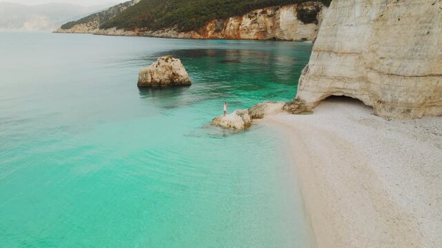 Woman standing on coastal rock overlooking clear turquoise sea waters in a peaceful Kefalonia cove