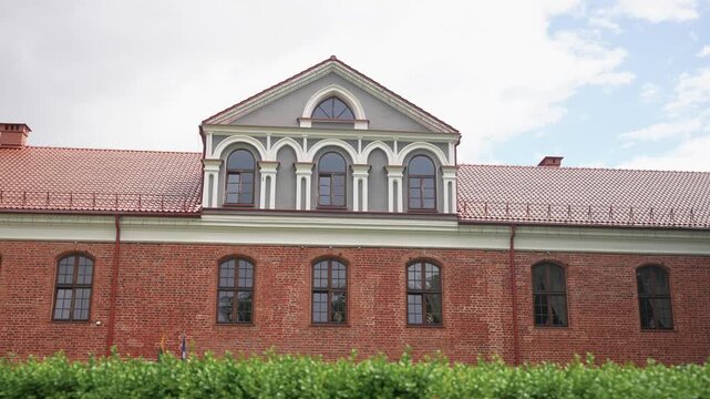 Smoothly tracking close-up shot of Raudondvaris Castle&rsquo;s ornate red brick facade, arched windows, and tiled roof, under bright daylight and soft clouds. No people, clean, stable framing.