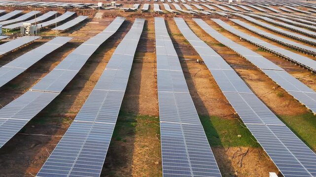Drone tracking left across a large photovoltaic solar farm with endless rows of solar panels producing renewable electricity and supporting sustainable energy infrastructure.