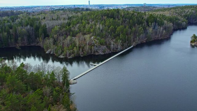 Aerial drone view of Stora Delsjon floating bridge crossing calm lake surrounded by Delsjo nature reserve forest near Gothenburg Sweden