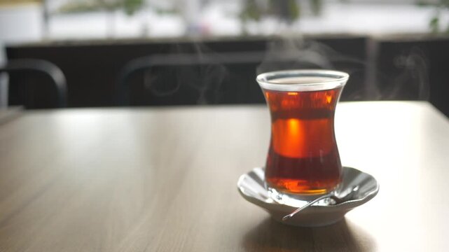 Steaming hot traditional Turkish tea in glass cup on wooden table in cafe