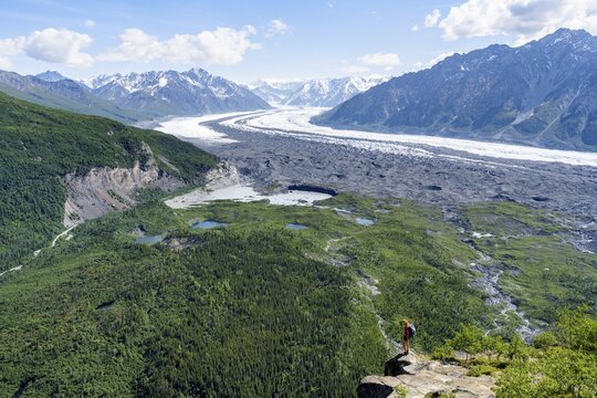 Young woman on a rocky outcrop enjoying the view, view of impressive mountain landscape with Matanuska glacier and glaciated mountain peaks, Lion's Head, Chugach Mountains, Alaska, USA