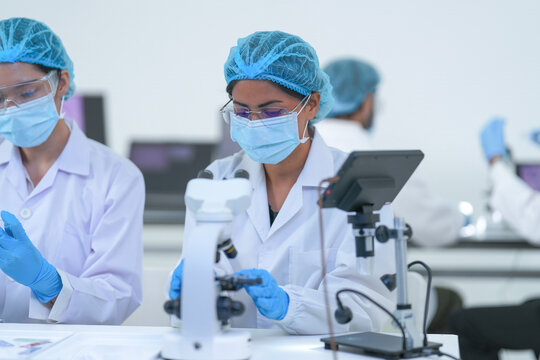 A research duo record microscope findings on a tablet in a clean modern science lab while wearing white lab coats and blue protective gloves and modern scientific innovation (No. 3274).