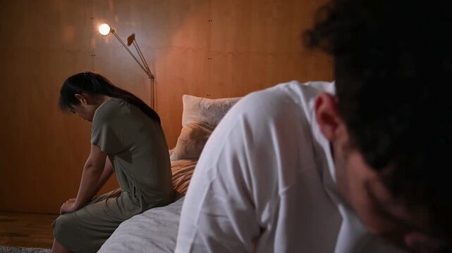 Unhappy couple sitting apart in bedroom after night argument and emotional distance