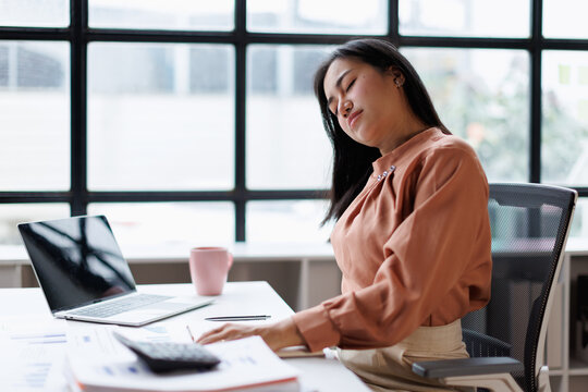 Woman feeling tired and stressed at her desk, experiencing neck pain and discomfort, taking a break from work due to fatigue and burnout from a sedentary office lifestyle
