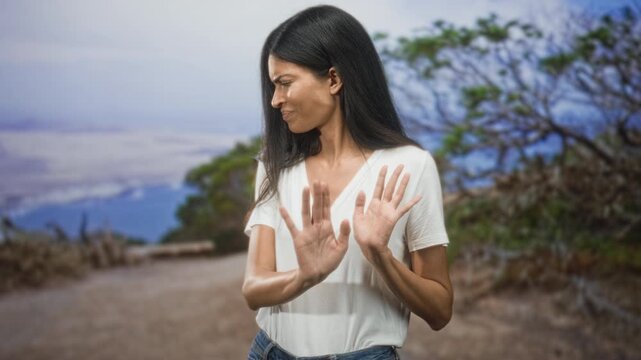 Woman with hands palms out pushed forward in a stop rejecting gesture on a forest path wearing white tshirt and jeans; rejection disgust avoidance.