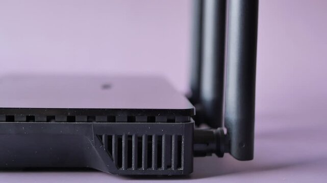 Side view of modern black wifi router with three antennas on purple surface
