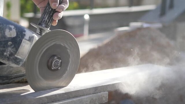 Worker cutting stone with angle grinder creating dust motion