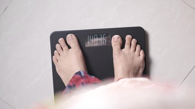 Woman steps onto digital weighing scale, measuring her weight in a dynamic top-down shot showing the numbers changing on the display