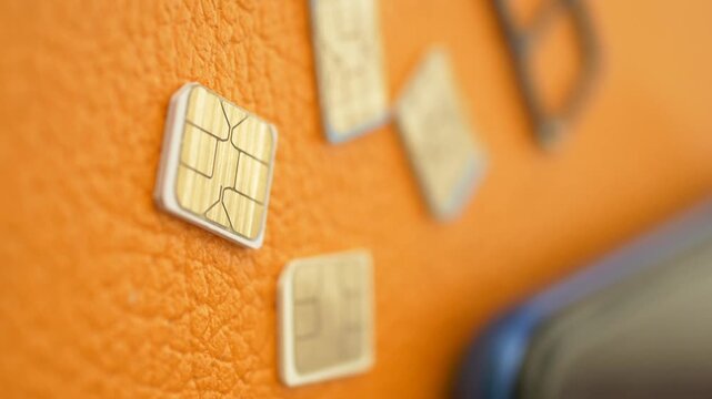 Close-up cinematic rack focus of various micro sim cards and sim tray on orange leather surface