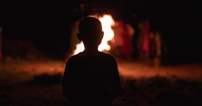 Silhouette of a young Samburu boy watching a traditional Adumu fire dance at night in Kenya. 