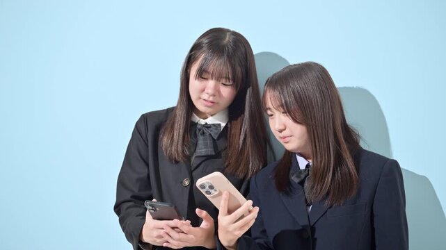 水色背景でスマートフォン(スマホ)を見る日本人女子中学生、女子高校生　2人で情報を共有する学校生活とコミュニケーション、スマホの安全な使い方イメージ