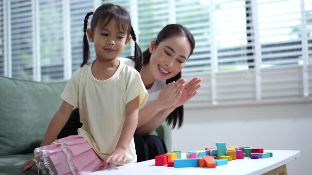 Mother and young daughter playing with colorful building blocks at home in a bright living room, spending time together and learning through play