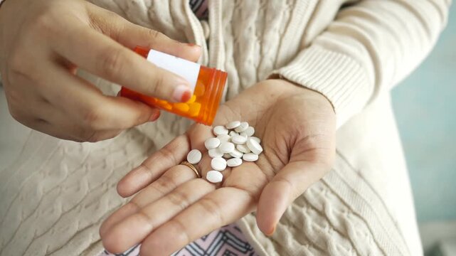 Close up video of a person pouring white pills from an orange bottle into their hand