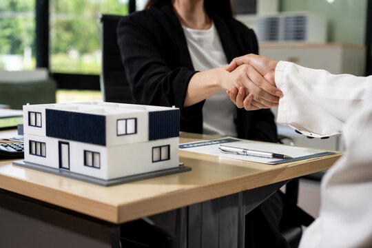 Business handshake over a table with a house model, suggesting a property deal, home buying, or agreement